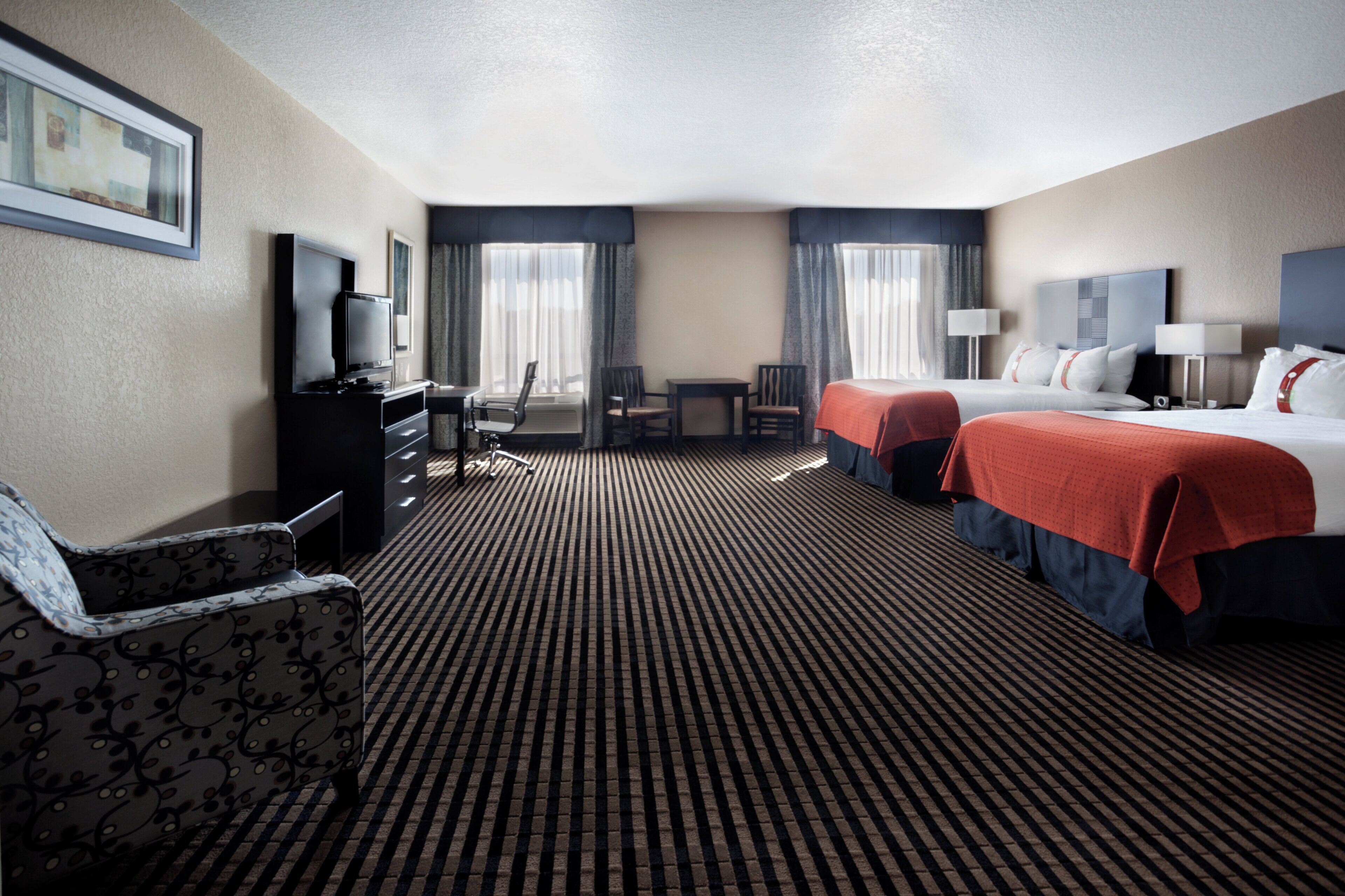 A hotel room with a bed, a desk, a chair, a television, and a window with curtains.