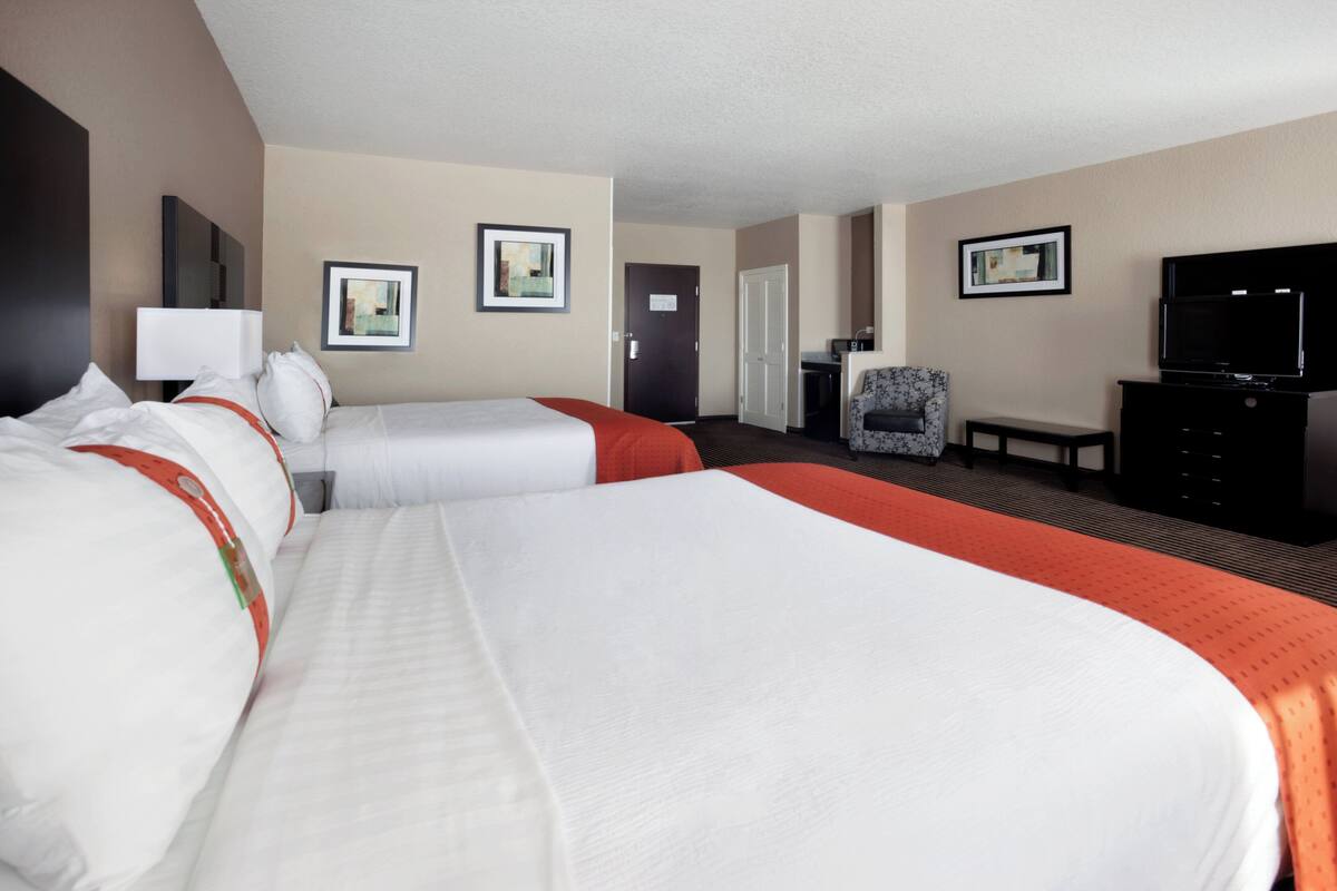 Ein Hotelzimmer mit zwei Betten, einem Fernseher, einem Schreibtisch und einem Sessel.