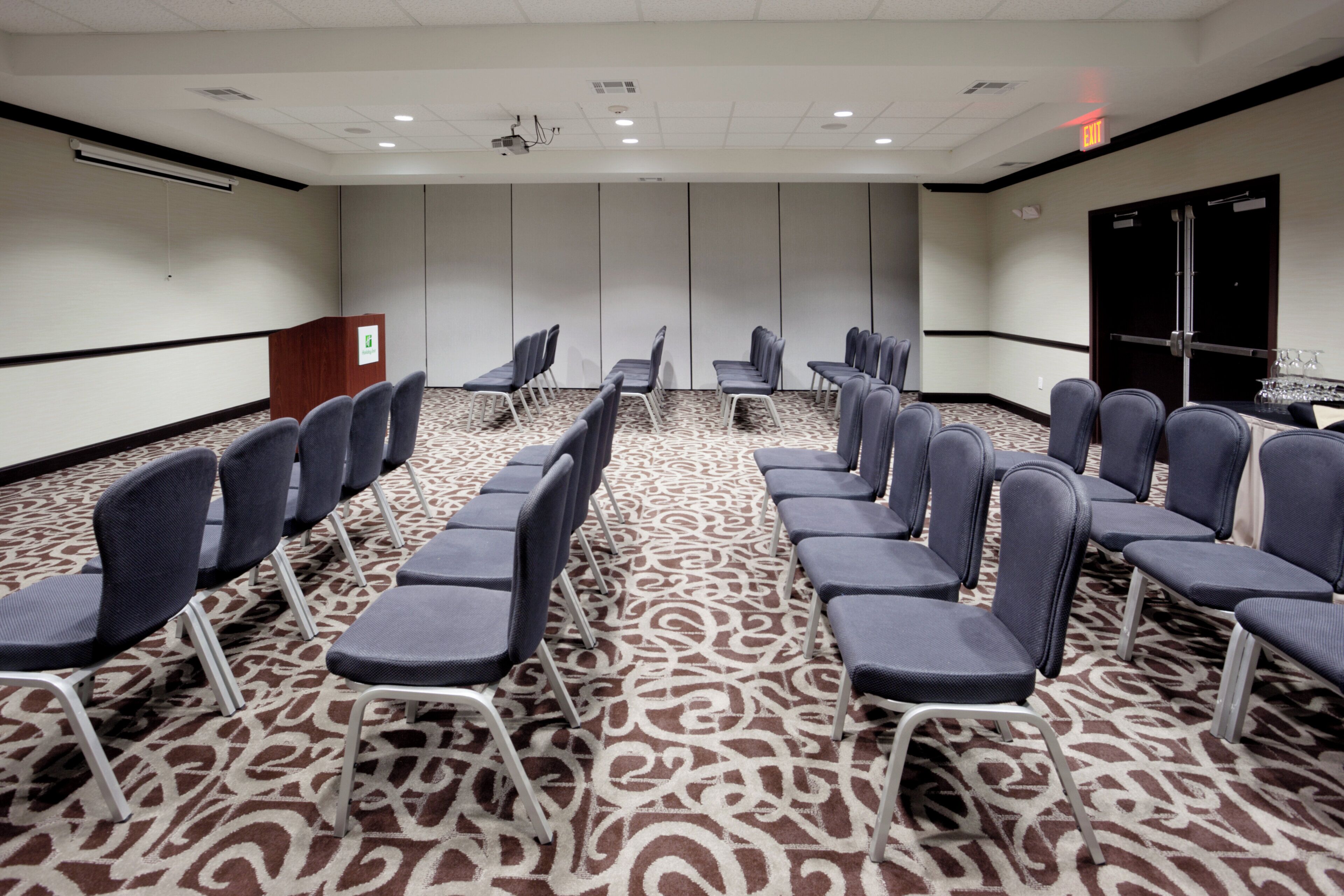 Un salón de conferencias con filas de sillas, un atril y una alfombra estampada.