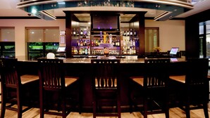 A bar area with a curved counter, multiple seating options, and a variety of bottles and glasses on shelves. - Holiday Inn San Antonio N - Stone Oak Area by IHG (San Antonio)