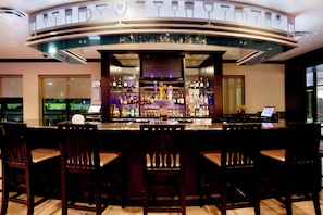 Zona de bar con mostrador curvo, distintas opciones de asientos y una variedad de botellas y vasos en estanterías.