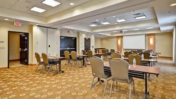 Un salón de conferencias con varias mesas y sillas, suelo alfombrado e iluminación en el techo.