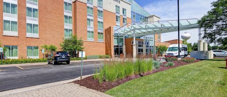 A modern hotel with a glass entrance, a brick facade, and a landscaped area with plants.