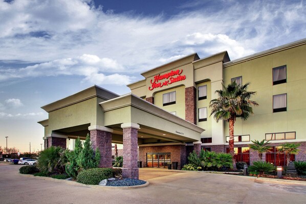 Edificio di Hampton Inn & Suites con ingresso coperto, palme e parcheggio.