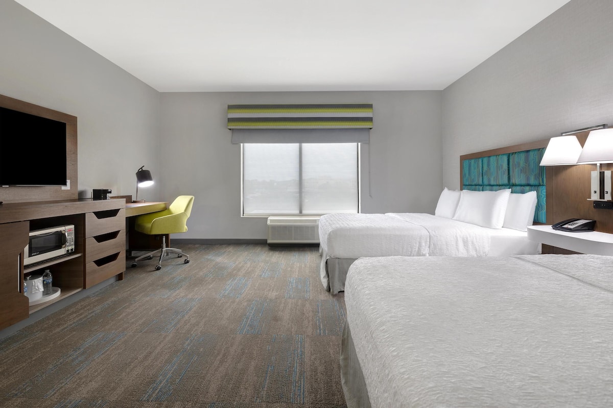 Habitación de hotel con dos camas, un escritorio con silla, televisión y ventana con vistas.