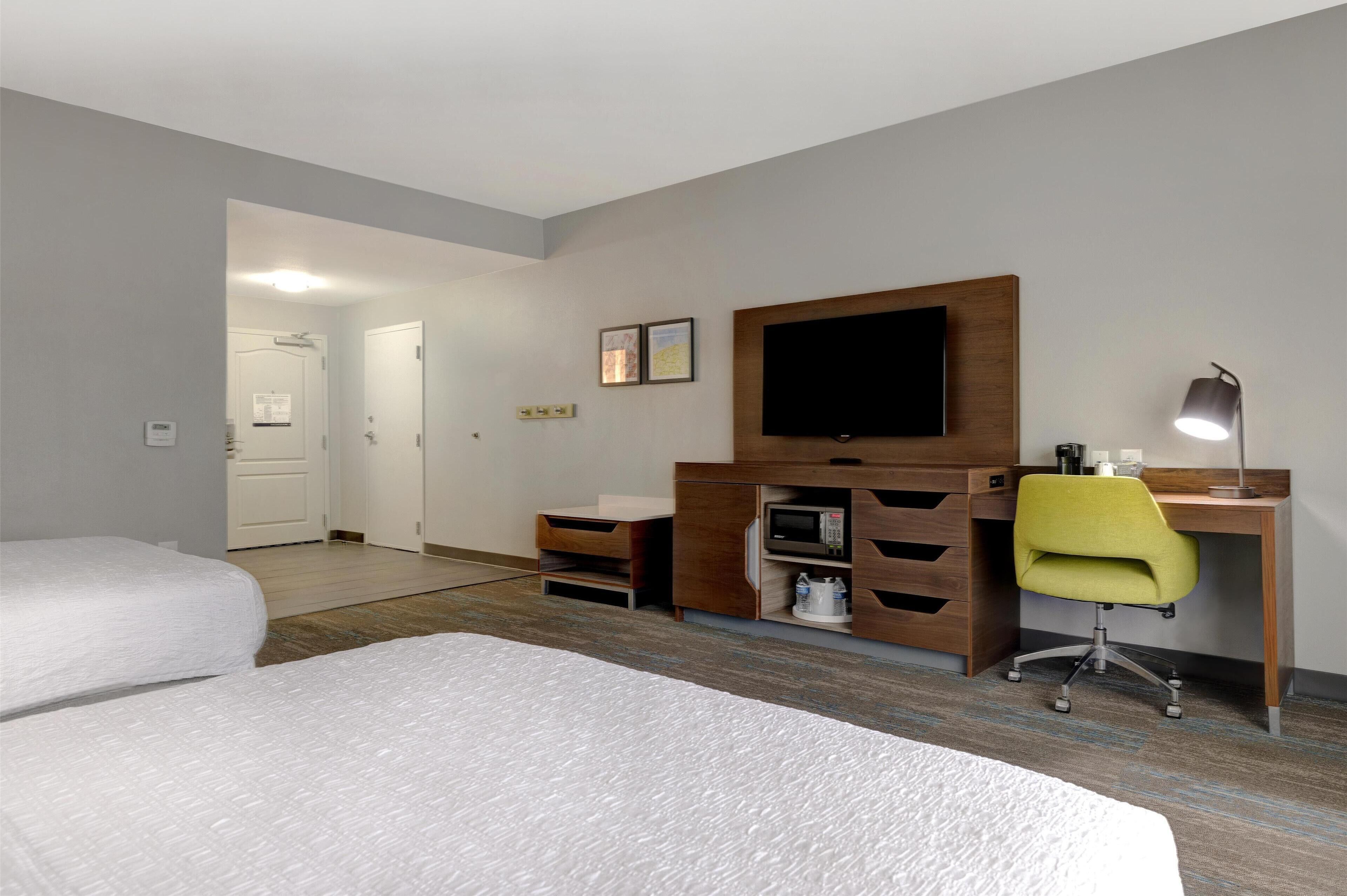 A hotel room with two beds, a desk with a computer, a TV, and a lamp.