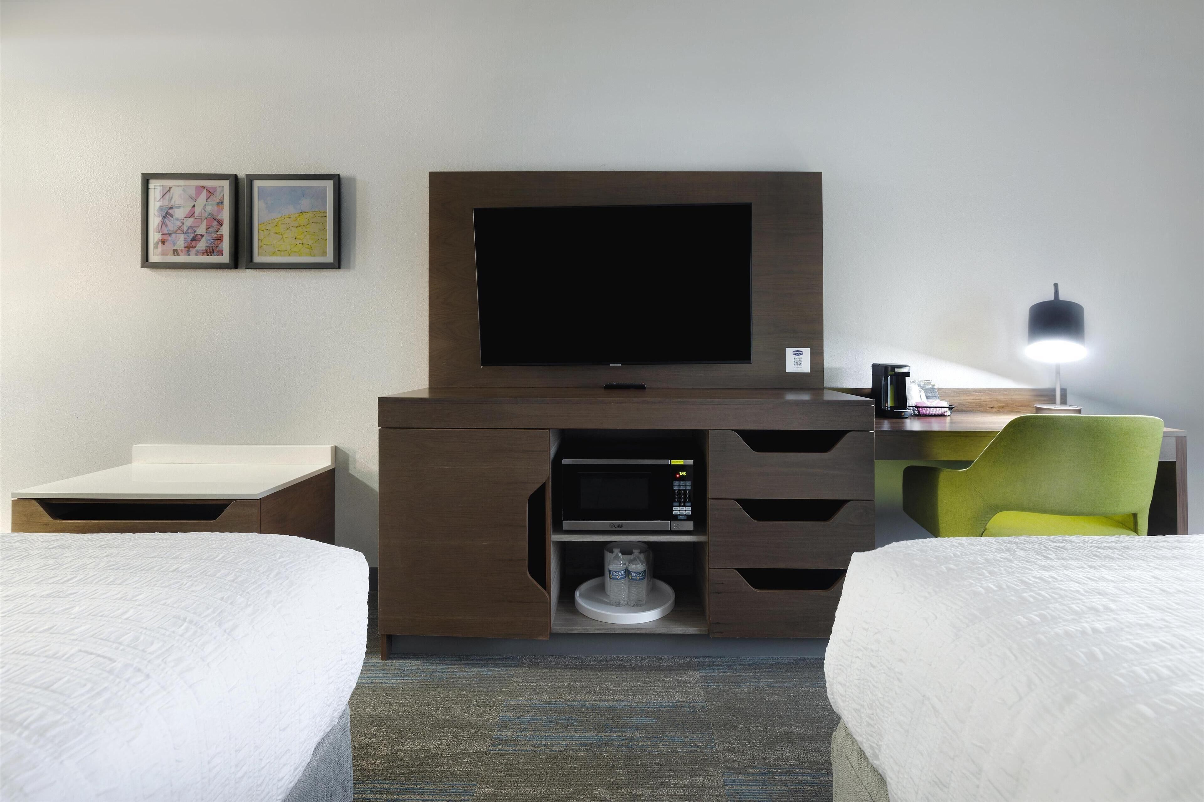 A hotel room with a bed, a desk with a computer, a flat-screen TV, a microwave, and a green chair.