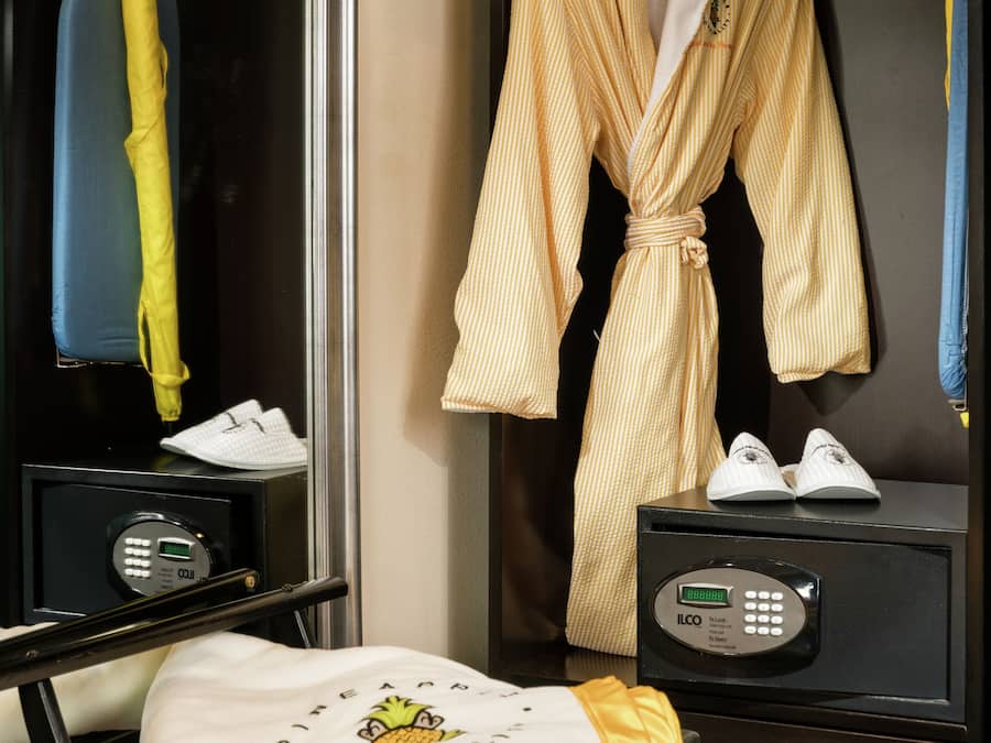 Une chambre d’hôtel avec un peignoir accroché au mur, une paire de chaussures posée sur une table et une serviette pliée sur une chaise.