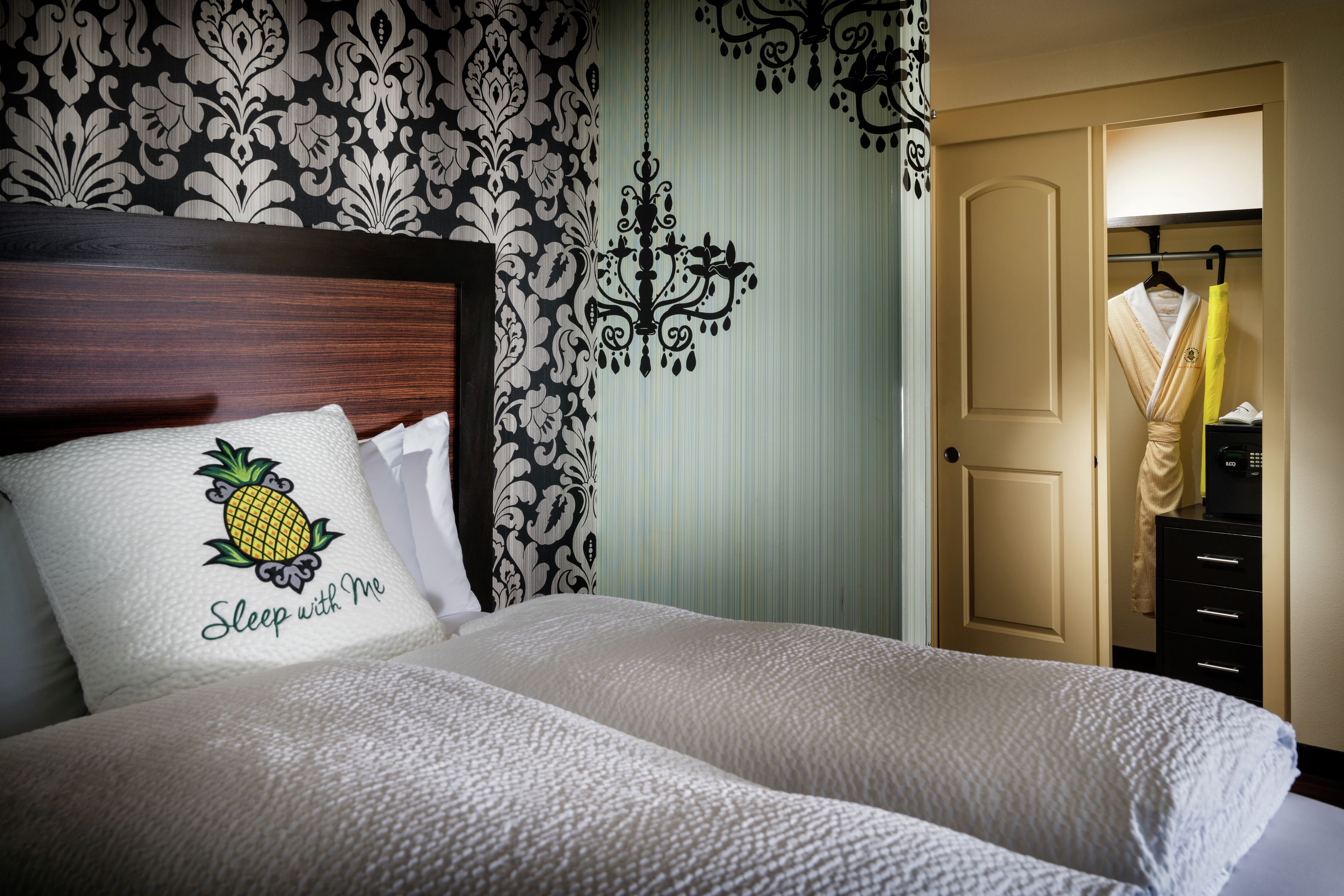 Una cama bien tendida con un cojín que tiene un diseño de piña y el texto 'Sleep with Me'.