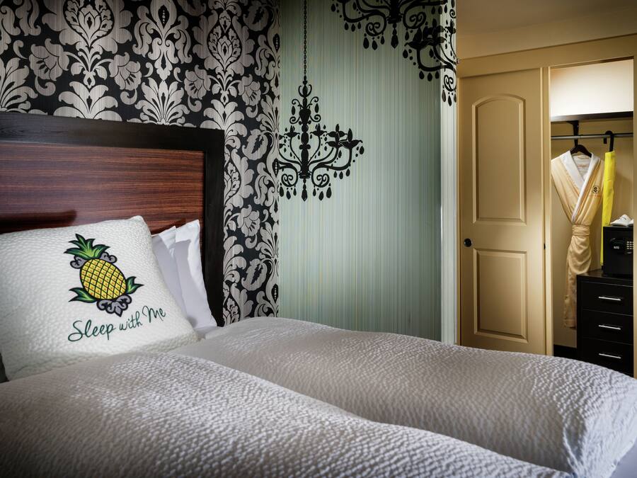 Una cama bien tendida con un cojín que tiene un diseño de piña y el texto 'Sleep with Me'.