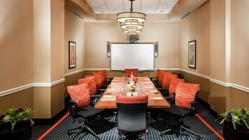 A conference room with a long table, red chairs, a whiteboard, and a chandelier.