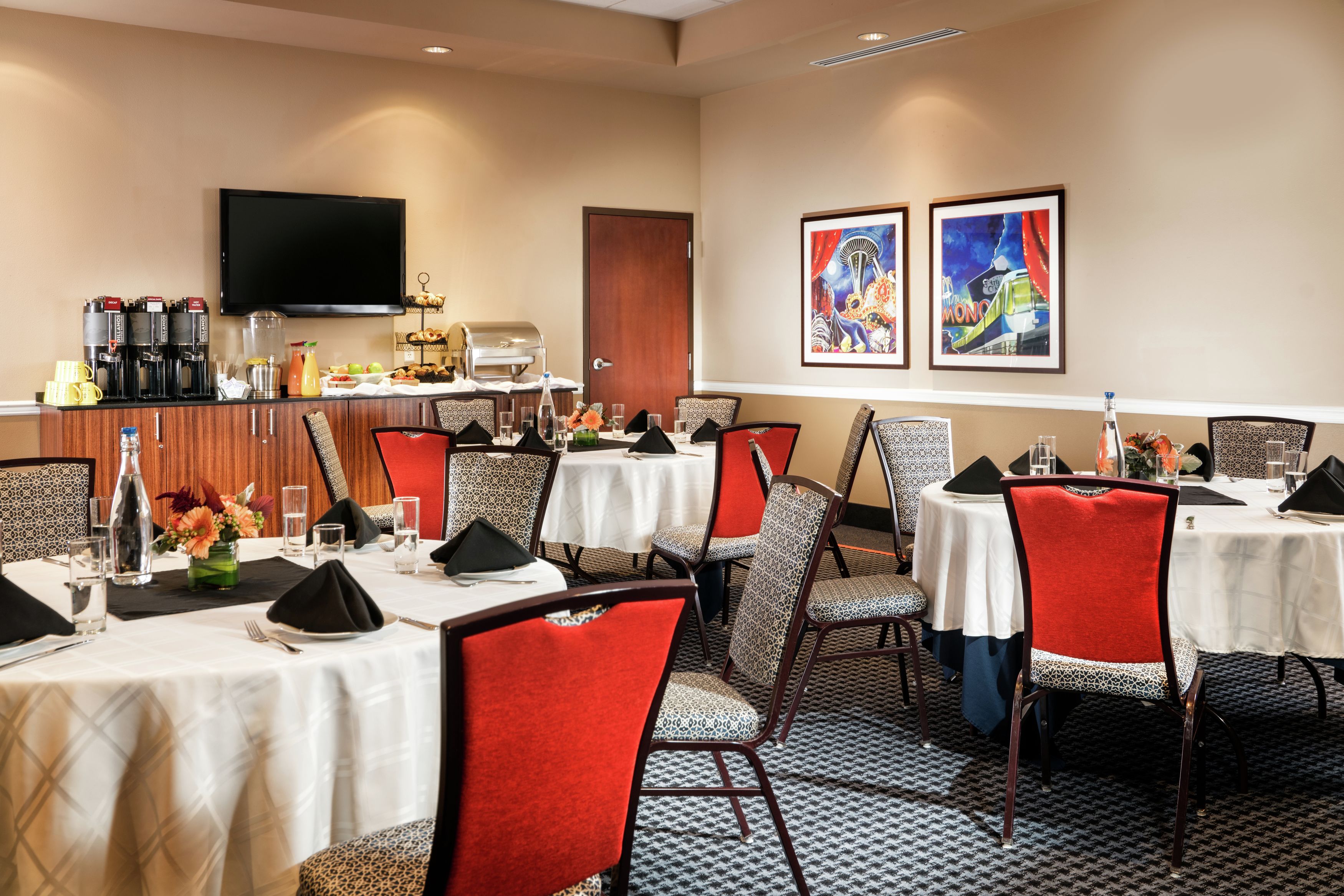 A hotel dining area with multiple tables and chairs, a coffee station, and artwork on the walls.