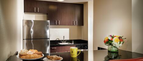 A modern kitchen with dark wooden cabinets, stainless steel appliances, and a dining table with a yellow mug and a floral arrangement.
