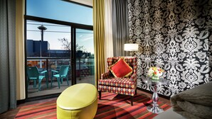 A hotel room with a large window, a patterned wallpaper, a colorful armchair, a small table with a lamp, and a yellow ottoman. - Staypineapple, The Maxwell Hotel, Seattle Center Seattle (Seattle)