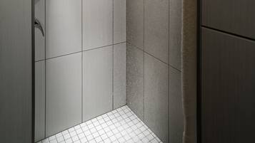 A modern shower with a handheld showerhead, tiled walls, and a vent on the ceiling.