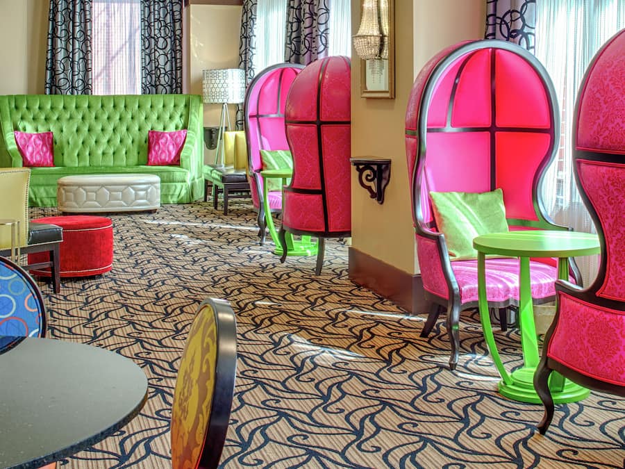 A room with a green sofa, pink chairs, and a patterned carpet.