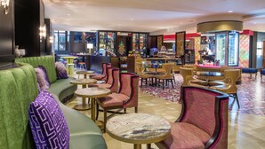 A hotel lobby with a green sofa, round tables, and chairs. There is a bar area with a refrigerator and shelves of snacks. - Staypineapple, The Maxwell Hotel, Seattle Center Seattle (Seattle)