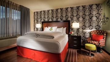 A hotel room with a large bed, a nightstand, a chair, and a patterned wallpaper.