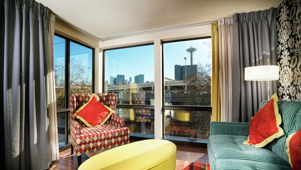A modern living room with large windows, a yellow ottoman, a green sofa, and a patterned armchair. - Staypineapple, The Maxwell Hotel, Seattle Center Seattle (Seattle)