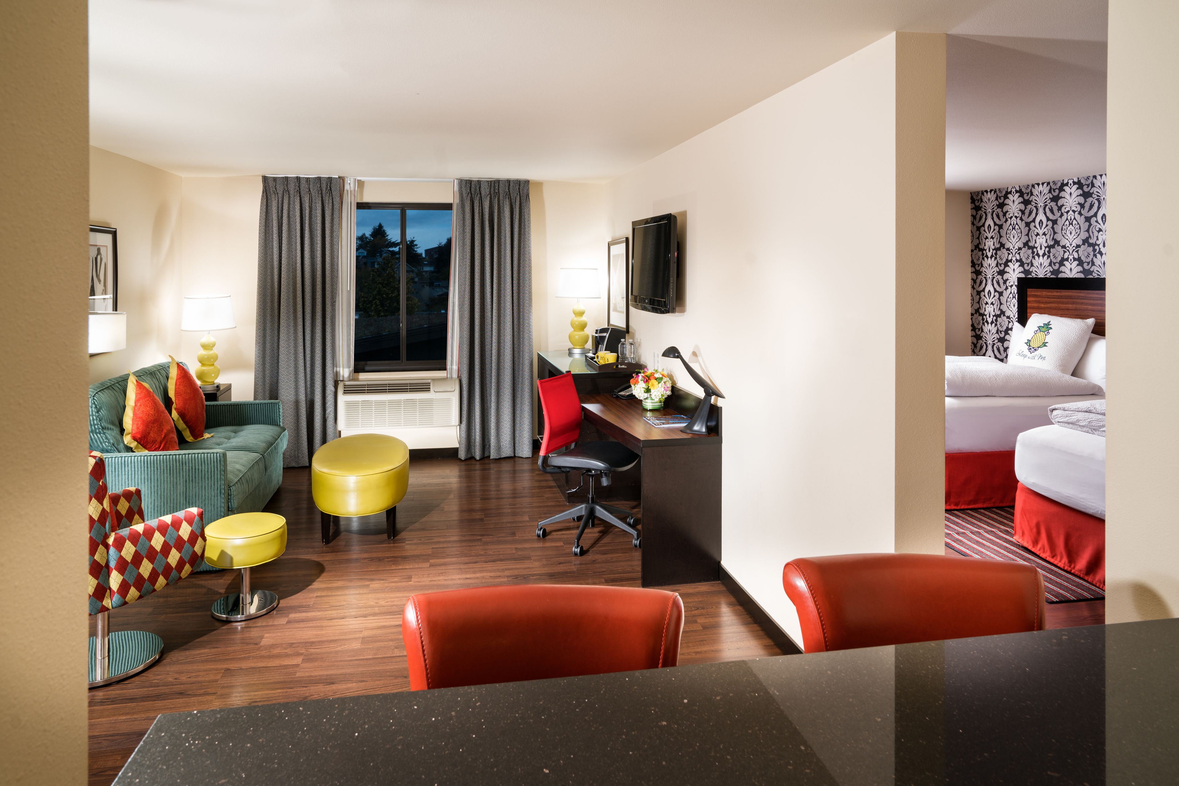 A hotel room with a sofa, a desk, a chair, a bed, and a TV.