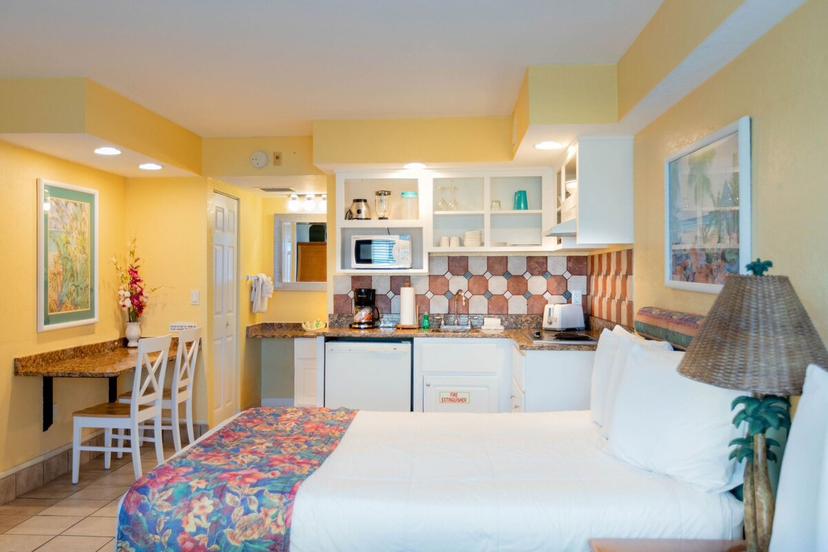 A compact hotel room with a bed, a small kitchenette, a dining area, and a bathroom.
