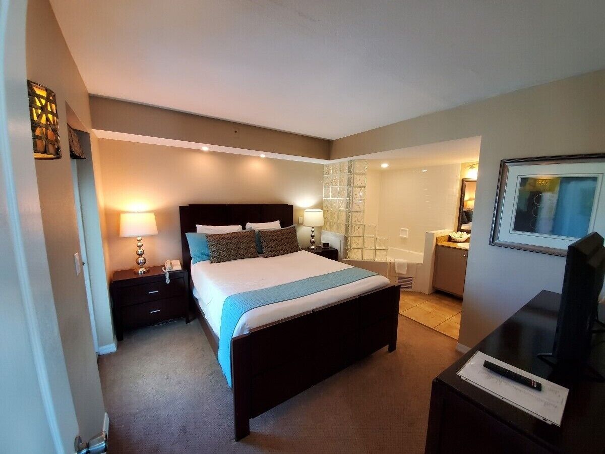 A hotel room with a large bed, bedside tables, a desk, and a television.