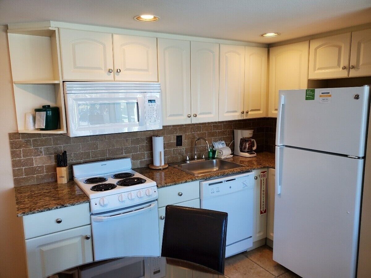 A compact kitchen with white cabinets, a stove, a microwave, and a refrigerator.