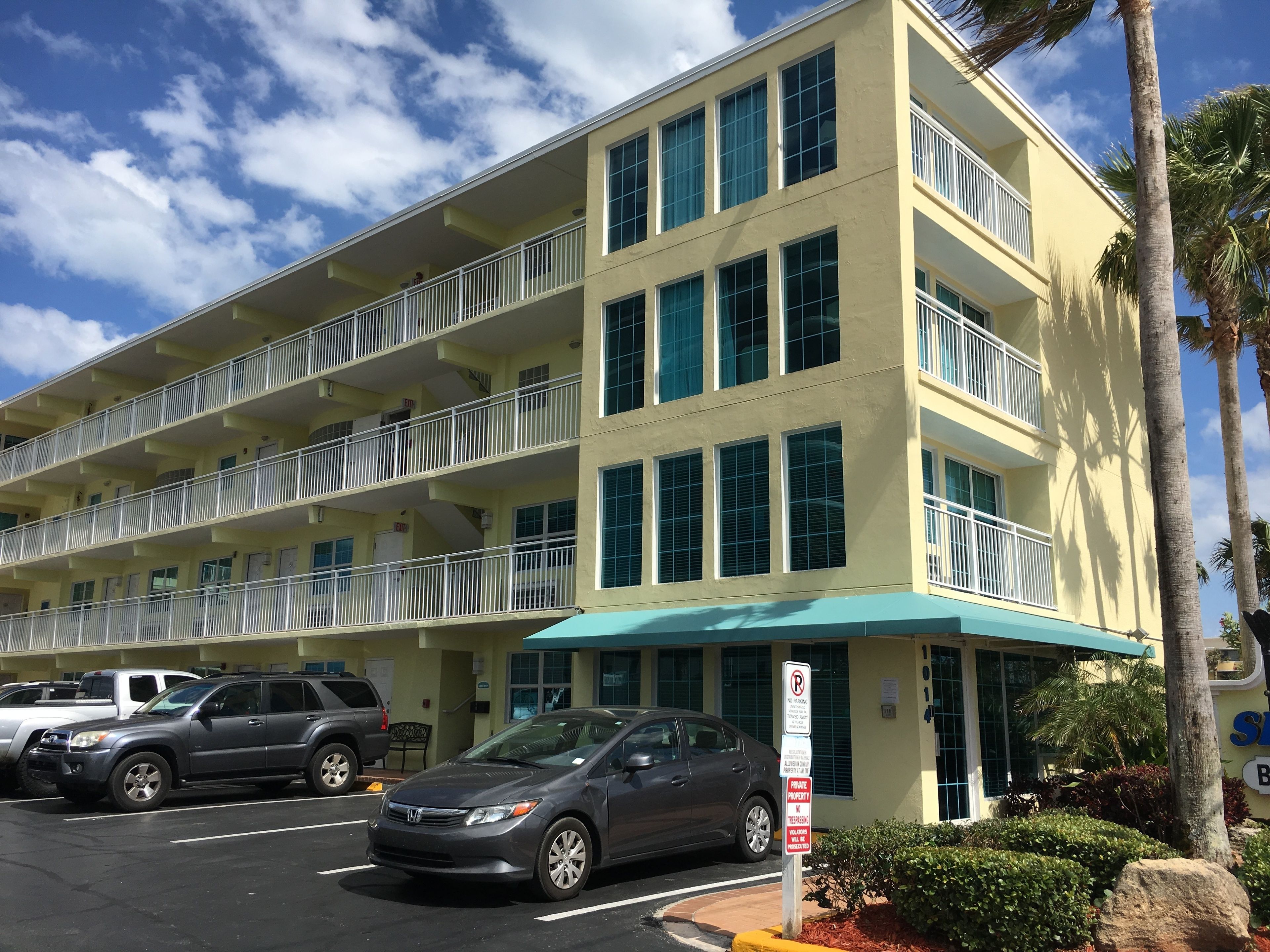 A multi-story hotel with balconies, a parking area, and a sign indicating no parking.