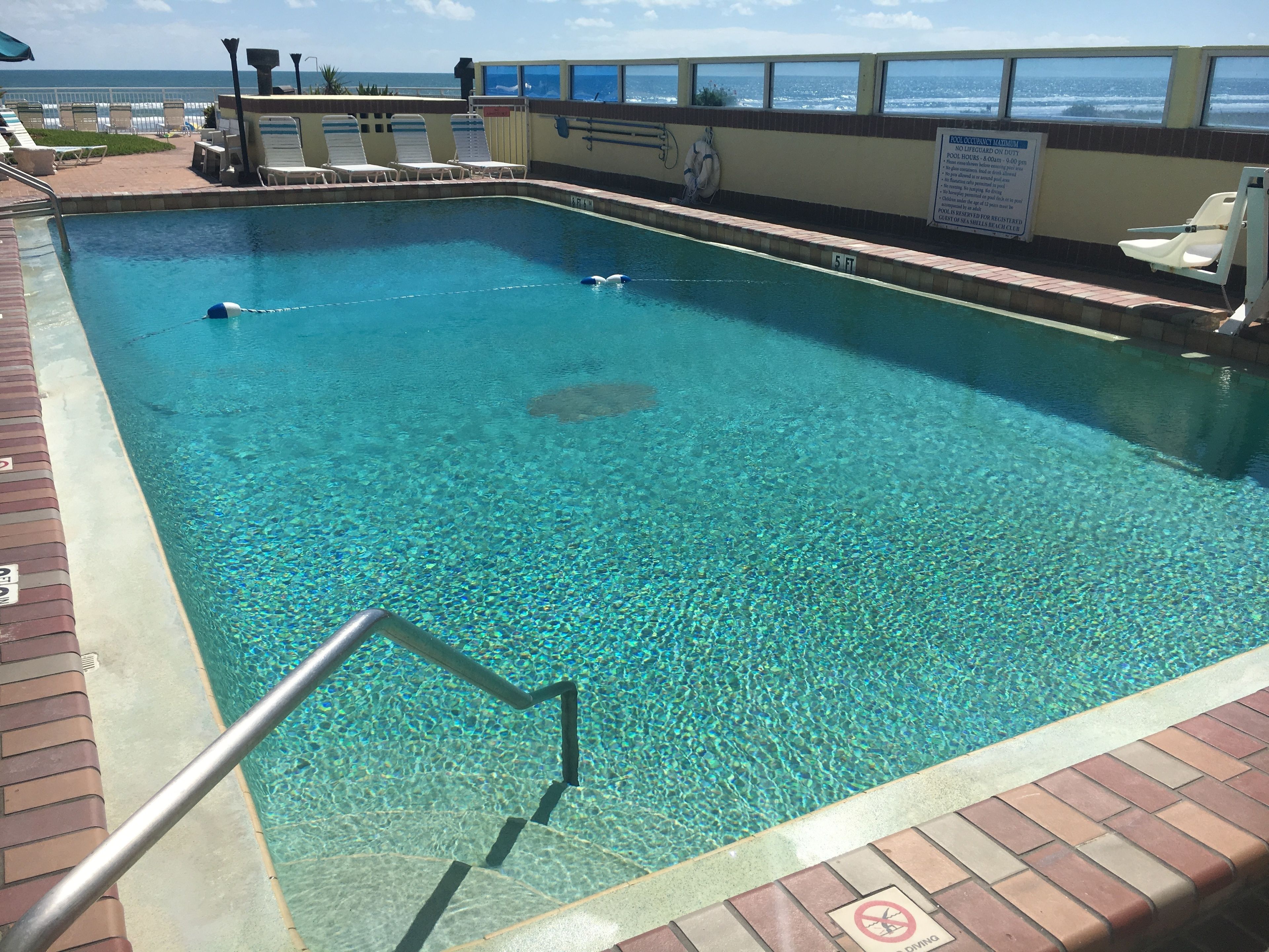 A rectangular pool with clear blue water, surrounded by a brick deck and a railing.