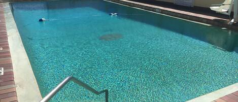 A rectangular pool with clear blue water, surrounded by a brick deck and a railing.