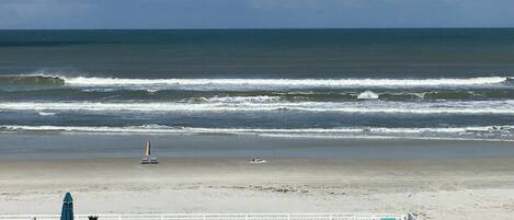 A beach view from a resort with lounge chairs, umbrellas, and a lifeguard tower.