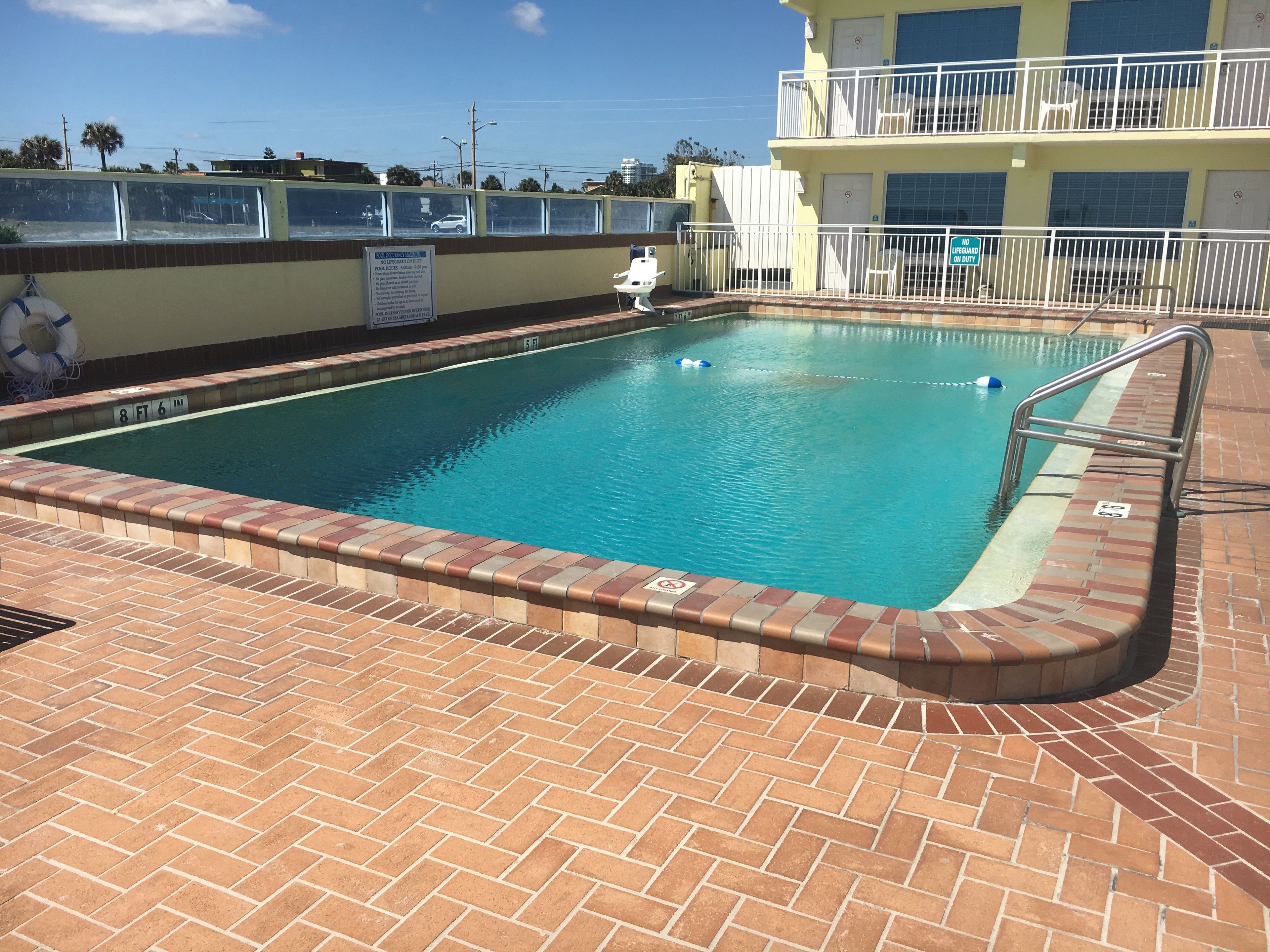 A rectangular swimming pool with a brick border and a metal handrail.