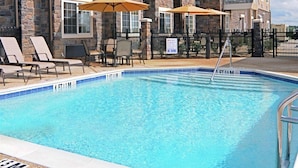A hotel pool area with lounge chairs and umbrellas, a stone facade, and a clear blue pool. - Microtel Inn & Suites by Wyndham Opelika (Opelika)