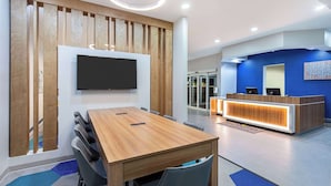 A modern hotel lobby with a wooden reception desk, a flat-screen TV mounted on the wall, and a conference table with chairs. - Microtel Inn & Suites by Wyndham Opelika (Opelika)
