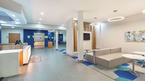 A modern reception area with a reception desk, seating area, and a large wall-mounted TV. - Microtel Inn & Suites by Wyndham Opelika (Opelika)