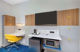 Habitación de hotel compacta con kitchenette, un pequeño escritorio con silla, televisor de pantalla plana y microondas.