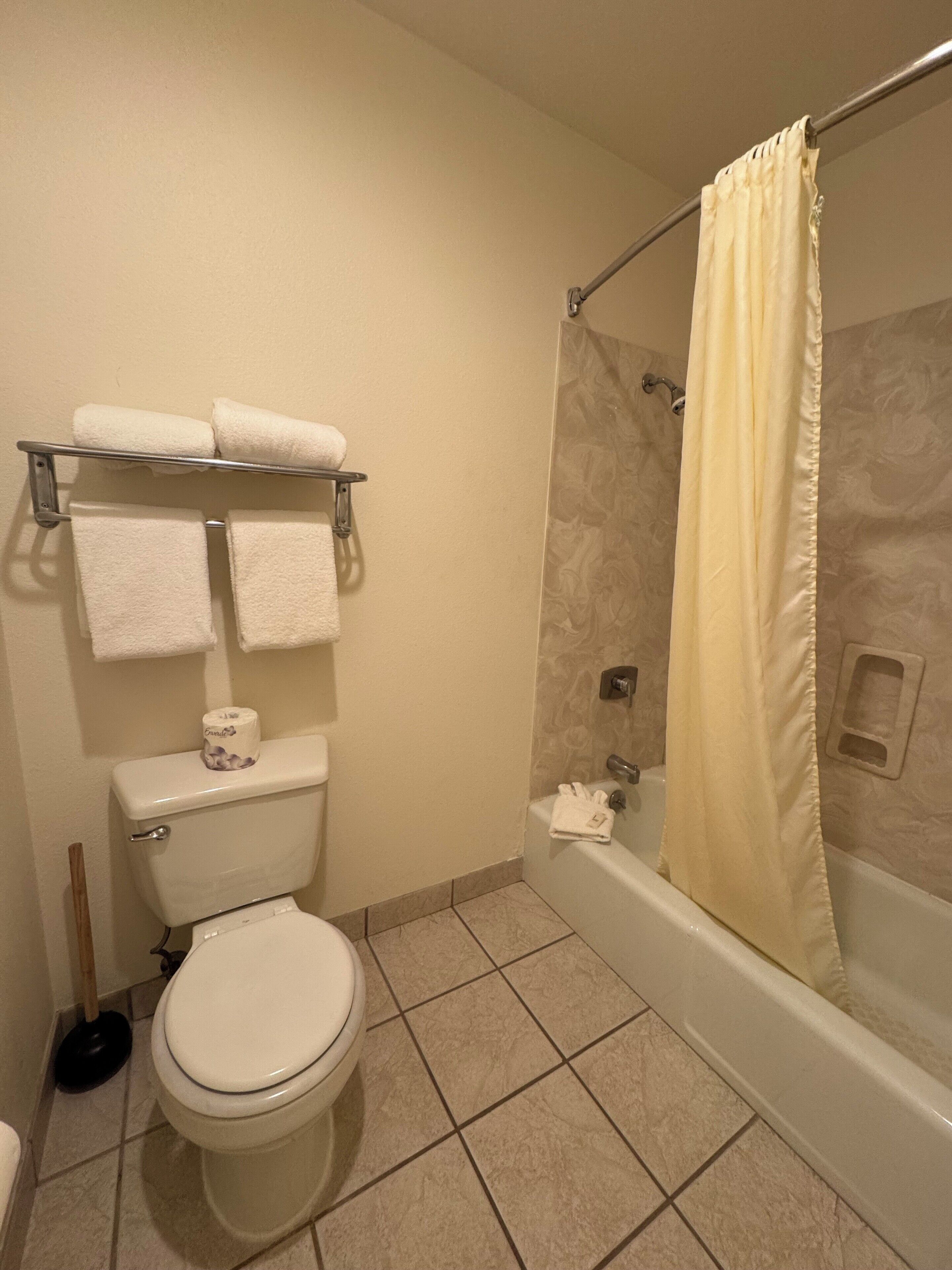 Et badeværelse med toilet, bruser med gardin og et håndklædestativ med håndklæder.