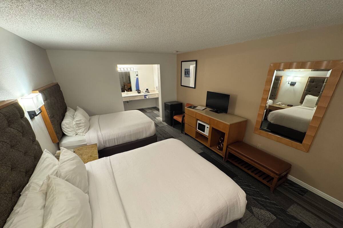 Habitación de hotel con dos camas, un escritorio con televisor, un espejo y una pequeña zona de estar.