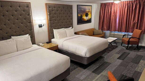 Quarto de hotel com duas camas, um sofá, uma poltrona, um quadro e uma janela com cortinas.