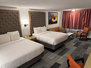 A hotel room with two beds, a sofa, a chair, a painting, and a window with curtains.