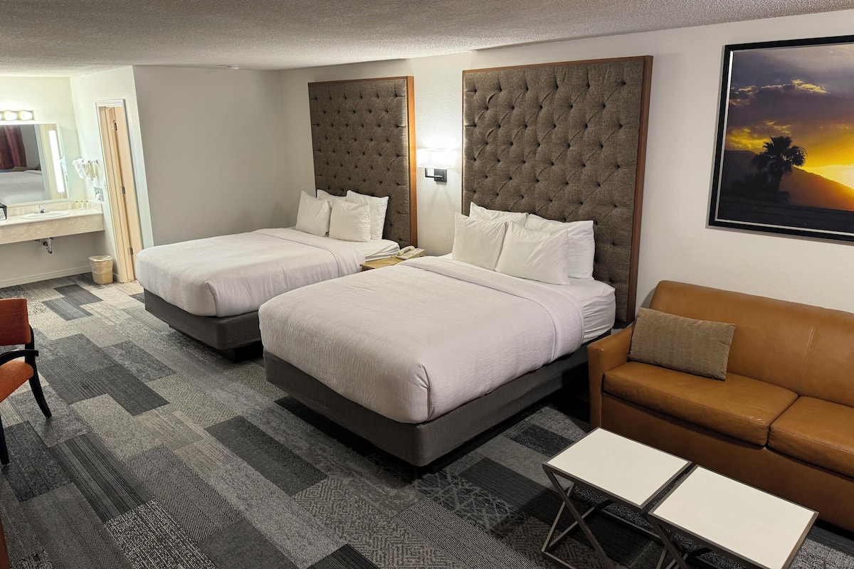 Habitación de hotel con dos camas, un sofá, una mesita y un cuadro en la pared.