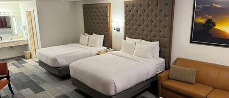 Habitación de hotel con dos camas, un sofá, una mesita y un cuadro en la pared.