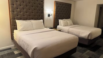 A hotel room with two beds, each with a tufted headboard and white bedding.