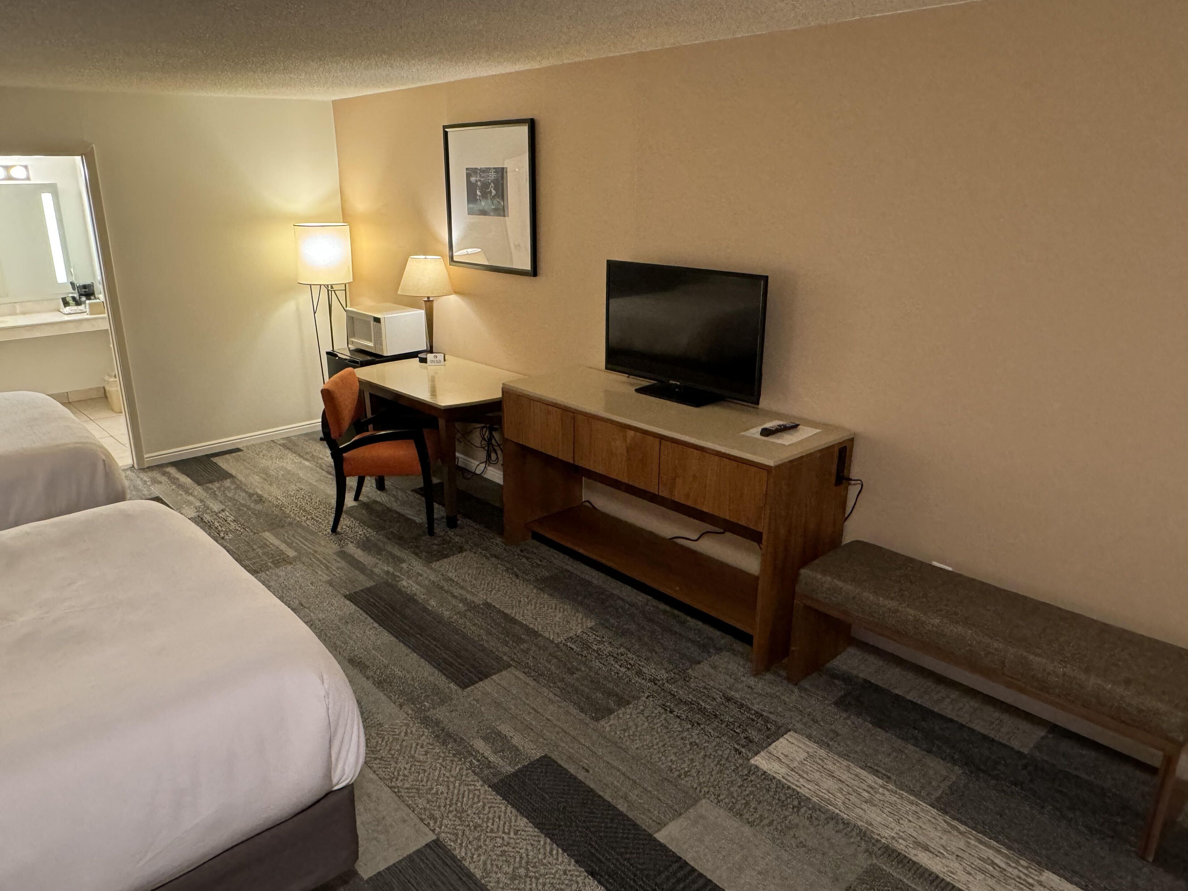 A hotel room with two beds, a desk with a television, a lamp, and a picture on the wall.
