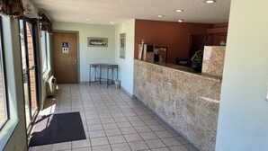Uma área de recepção com balcão de mármore, uma mesa pequena e uma porta com o sinal de acessibilidade para cadeiras de rodas.