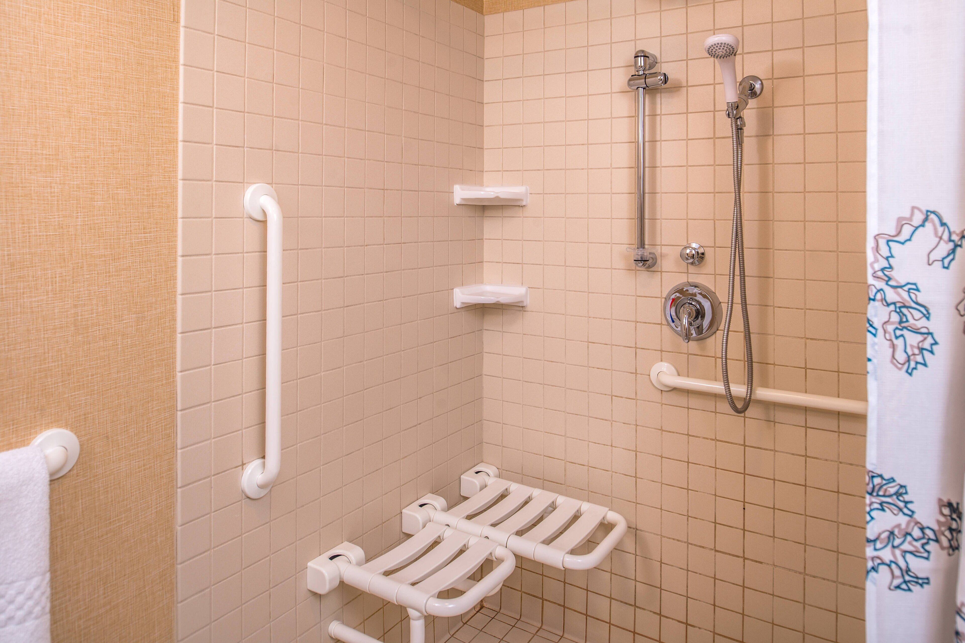 A small, tiled bathroom with a shower, grab bars, and a towel rack.