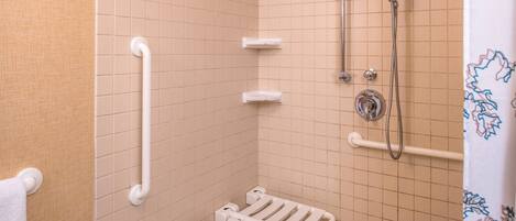 A small, tiled bathroom with a shower, grab bars, and a towel rack.