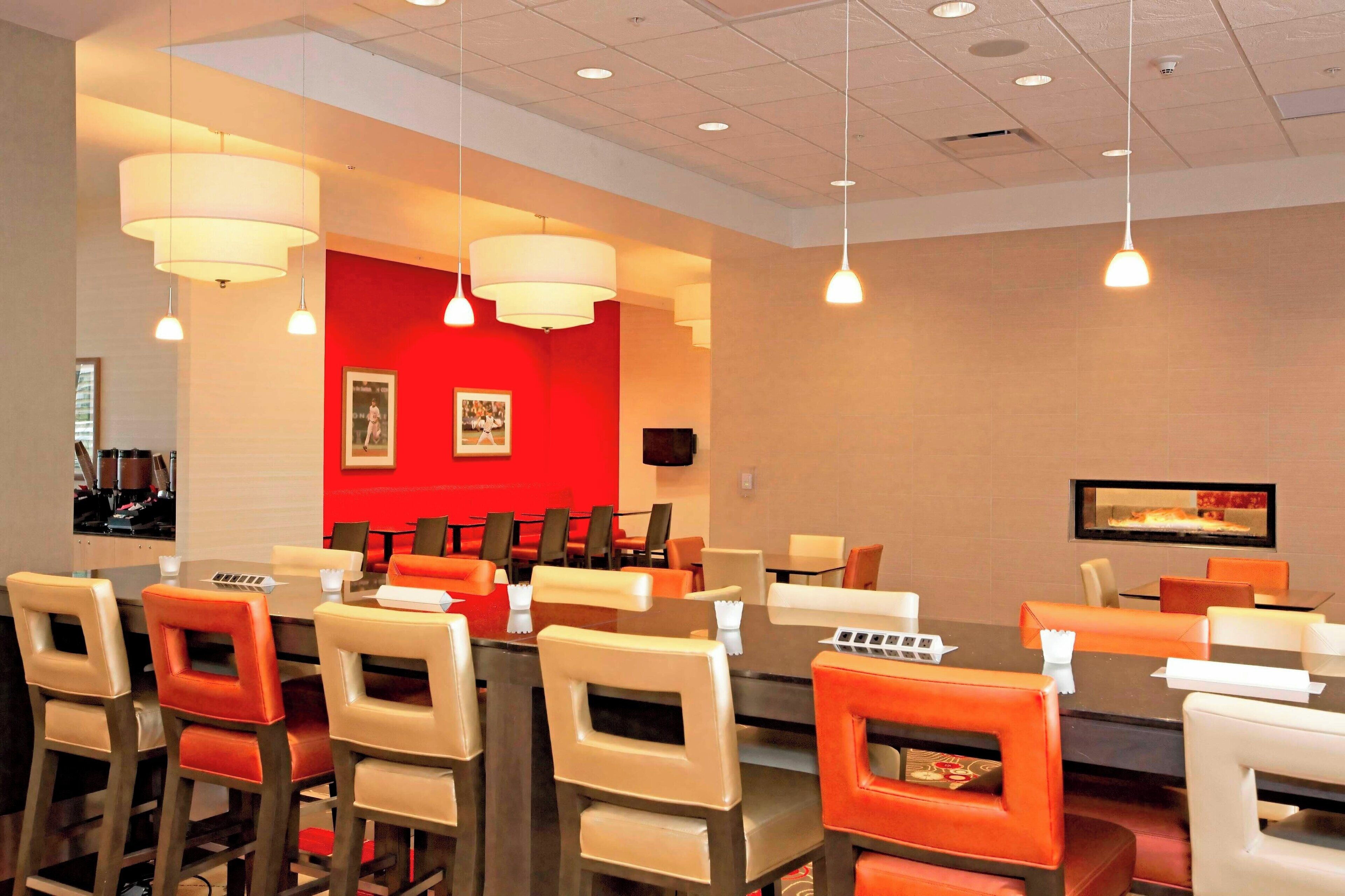 A restaurant with high tables and chairs, overhead lighting, and a red accent wall.