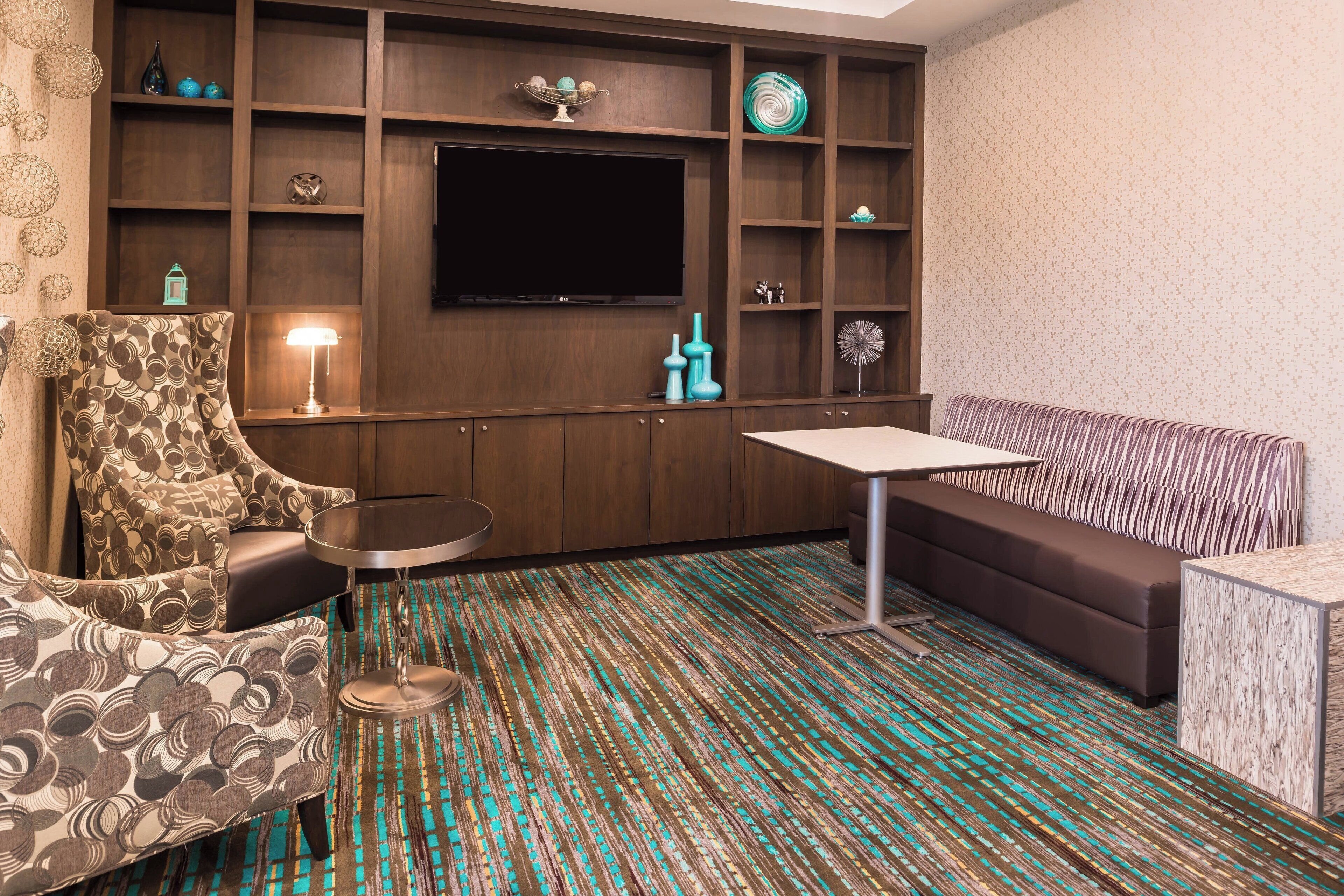 Ein modernes Wohnzimmer mit einer Couch, einem Sessel und einem kleinen Tisch. Ein Flachbildfernseher ist an der Wand montiert, und der Raum verfügt über einen Teppich mit Muster.
