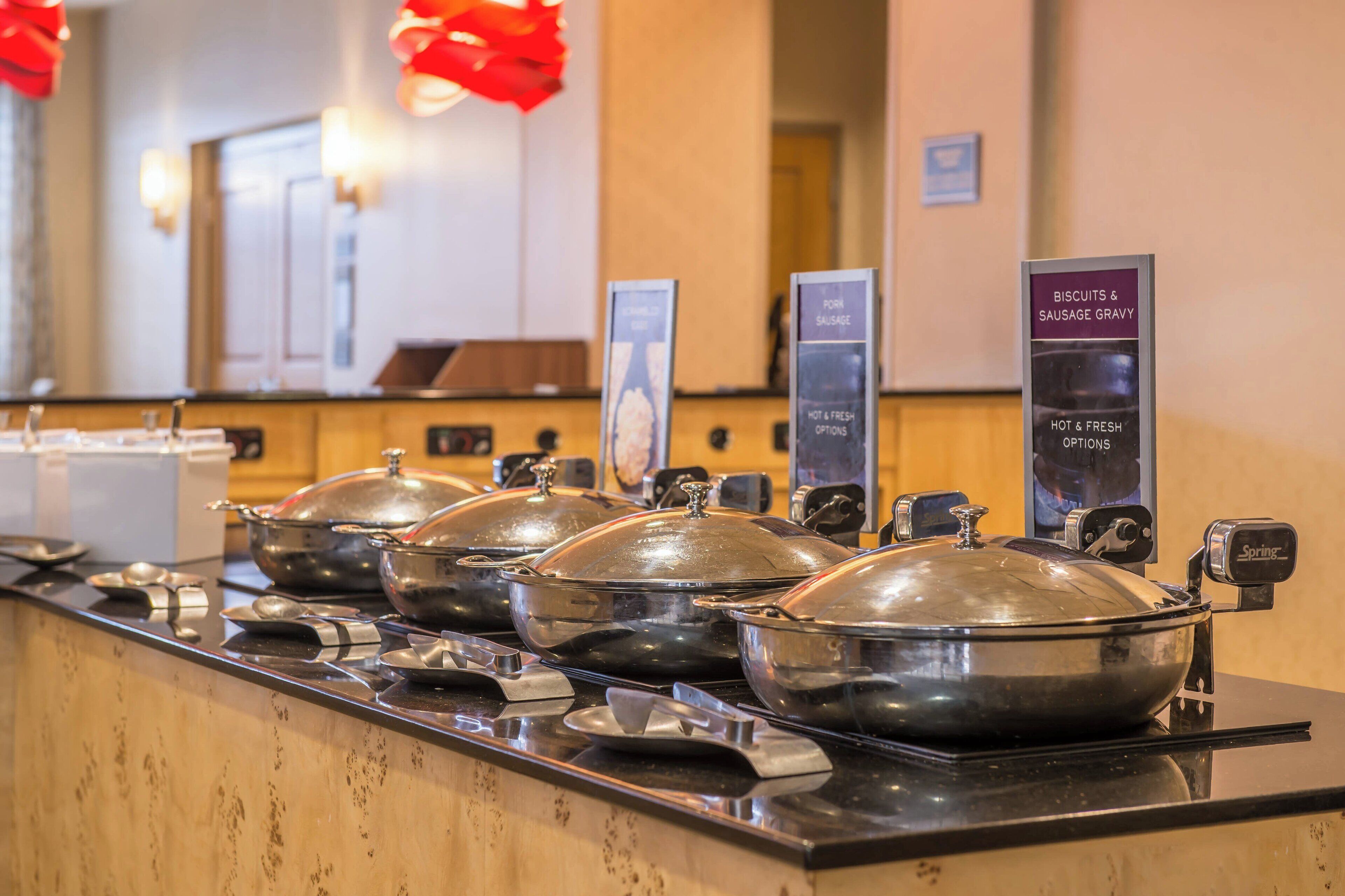A buffet setup with multiple covered serving stations, each labeled with different food options like biscuits, sausage, and gravy.